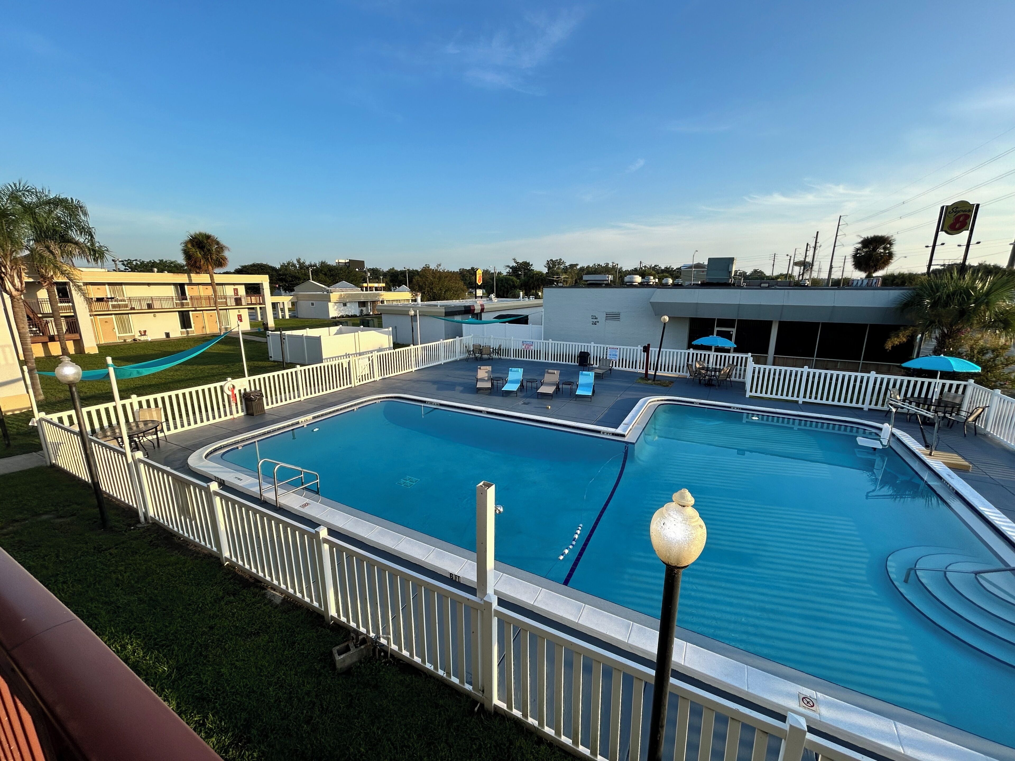 A swimming pool with a white deck and lounge chairs, surrounded by a white fence.