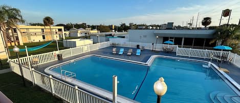 A swimming pool with a white deck and lounge chairs, surrounded by a white fence.