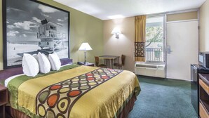 A hotel room with a bed, a desk, a chair, a television, a window with curtains, and a painting on the wall.