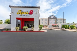 A hotel named 'Super 8' with a red entrance, a parking lot, and a building labeled 'The American Road Original' in the background. - Super 8 by Wyndham - Mesa/Gilbert (Mesa)