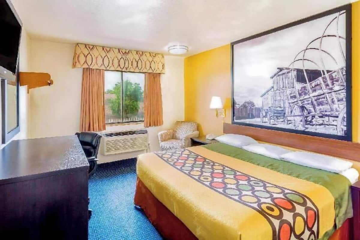Habitació d'hotel amb un llit, una taula de nit, una cadira, una finestra amb cortines i un quadre penjat a la paret.