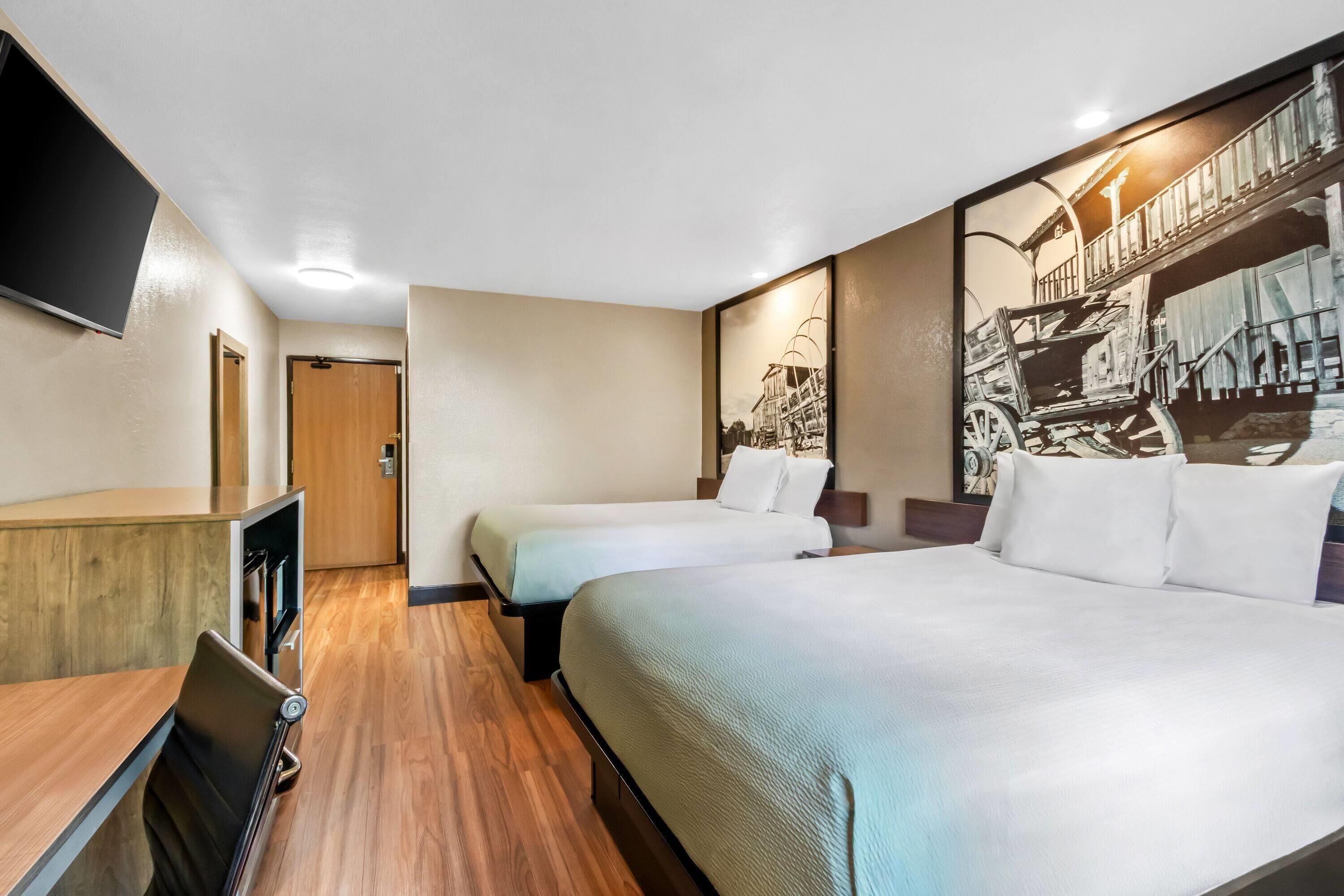 A hotel room with two beds, a desk, a TV, and a large wall mural.
