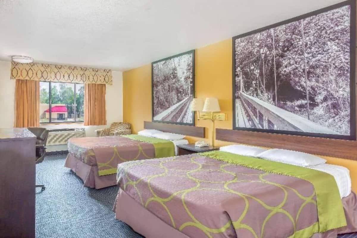 Habitació d'hotel amb dos llits, un escriptori, una cadira i una finestra amb cortines.