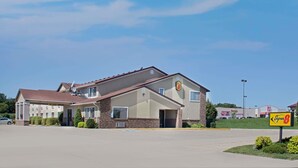 A Super 8 motel with a brick facade, a covered parking area, and a clear blue sky. - Super 8 by Wyndham Charles City (Charles City)