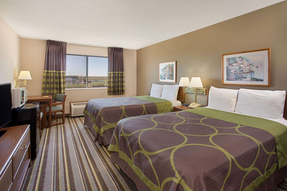 A hotel room with two beds, a desk, a chair, a TV, and a window with curtains.