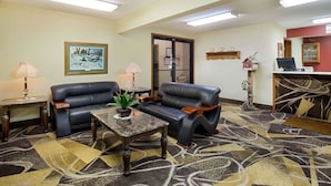A lobby with two leather sofas, a coffee table, a potted plant, a framed picture, and a reception desk. - Super 8 by Wyndham Charles City (Charles City)