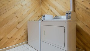 A laundry room with two white appliances, a wooden sloped ceiling, and white tiled flooring. - Super 8 by Wyndham Charles City (Charles City)