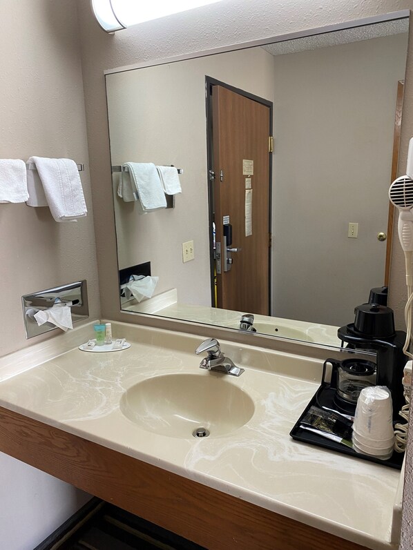 A hotel bathroom with a large sink, a mirror, a hairdryer, and towels on a rack.