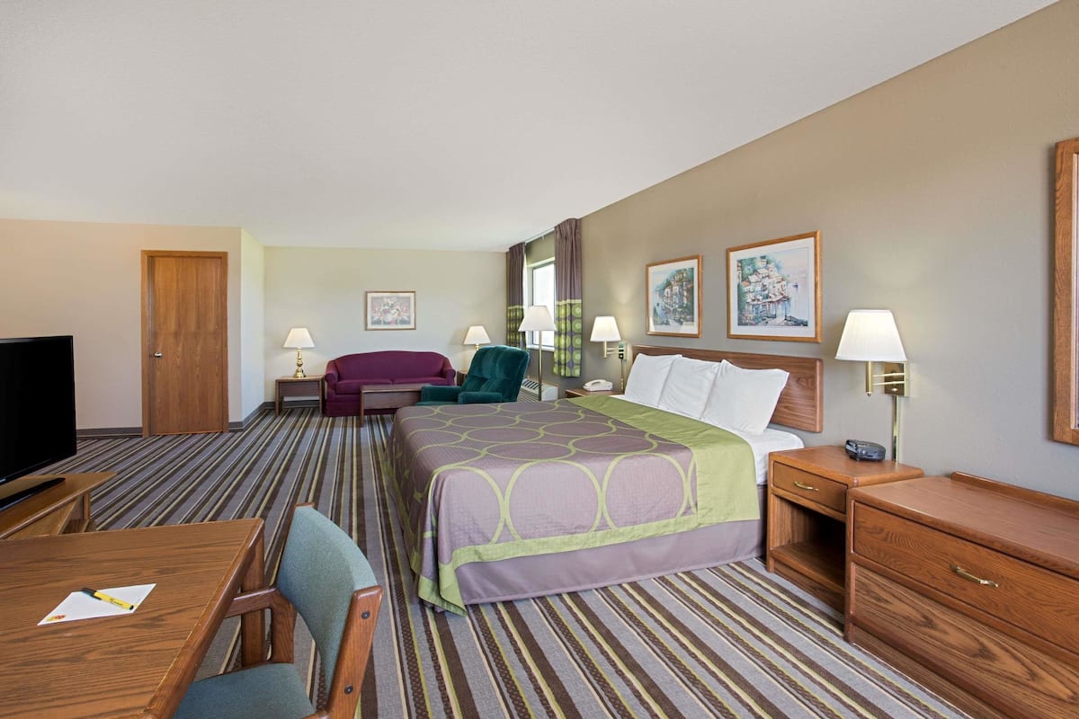 A hotel room with a bed, a desk, a TV, a chair, a lamp, and a nightstand.