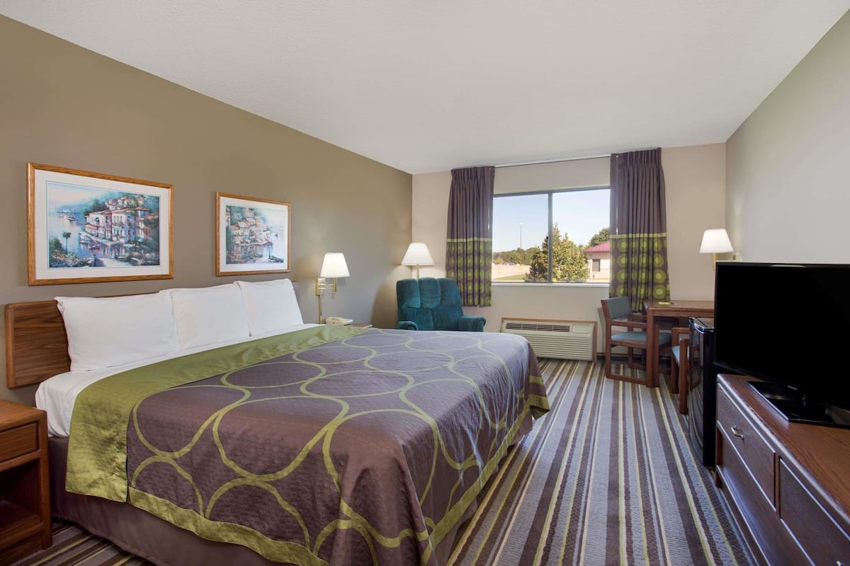 A hotel room with a bed, a desk with a chair, a television, and two paintings on the wall.