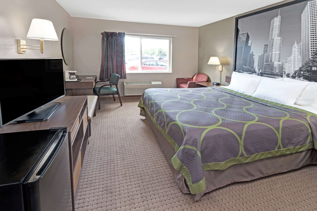 Ein Hotelzimmer mit Bett, Fernseher, Schreibtisch, Stuhl und einem Fenster mit Vorhängen.