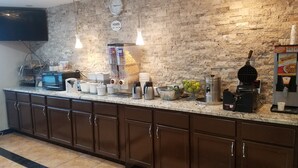 A kitchen area with a stone wall, a clock, a microwave, a waffle maker, and a coffee machine. - Super 8 by Wyndham Chicago O'Hare Airport (Elk Grove Village)