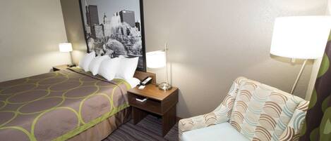 Quarto de hotel com duas camas, uma cadeira, uma mesa com abajur e uma grande imagem emoldurada de um panorama urbano na parede.