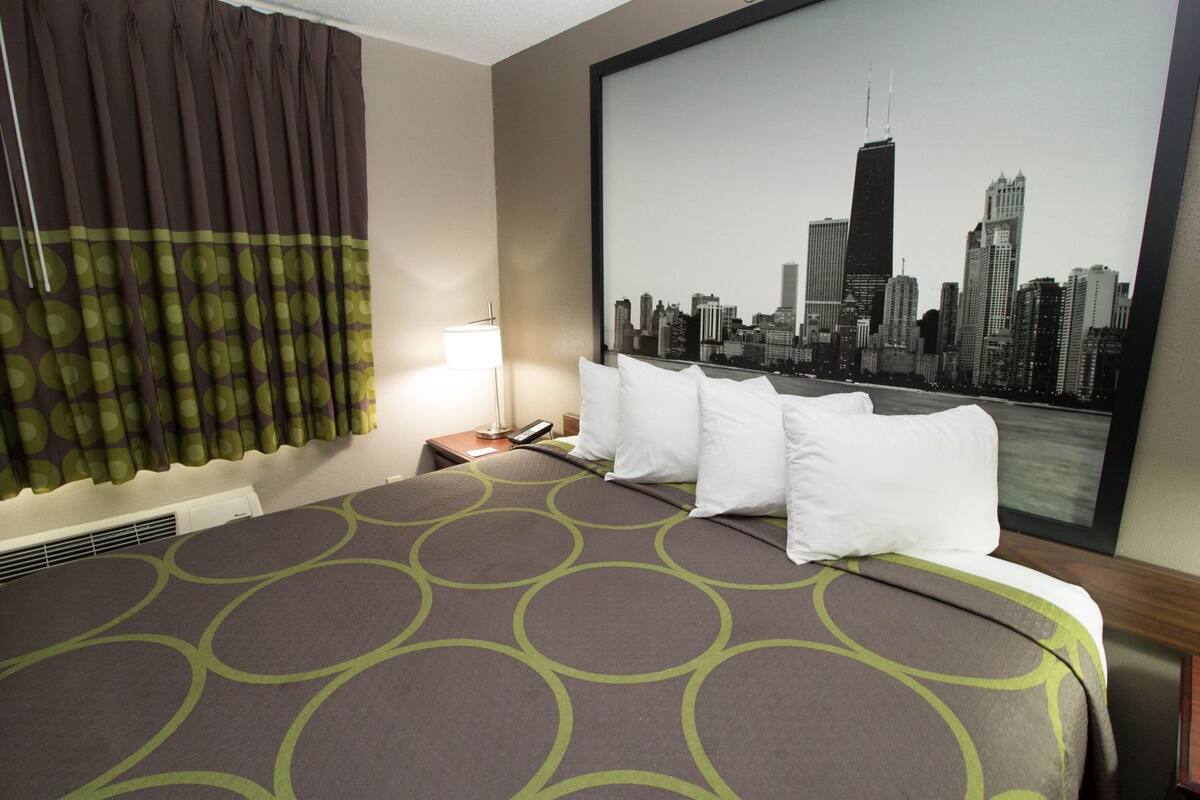 Ein Hotelzimmer mit Bett, Blick auf die Stadt, einer Lampe und einem Fenster mit Vorhängen.