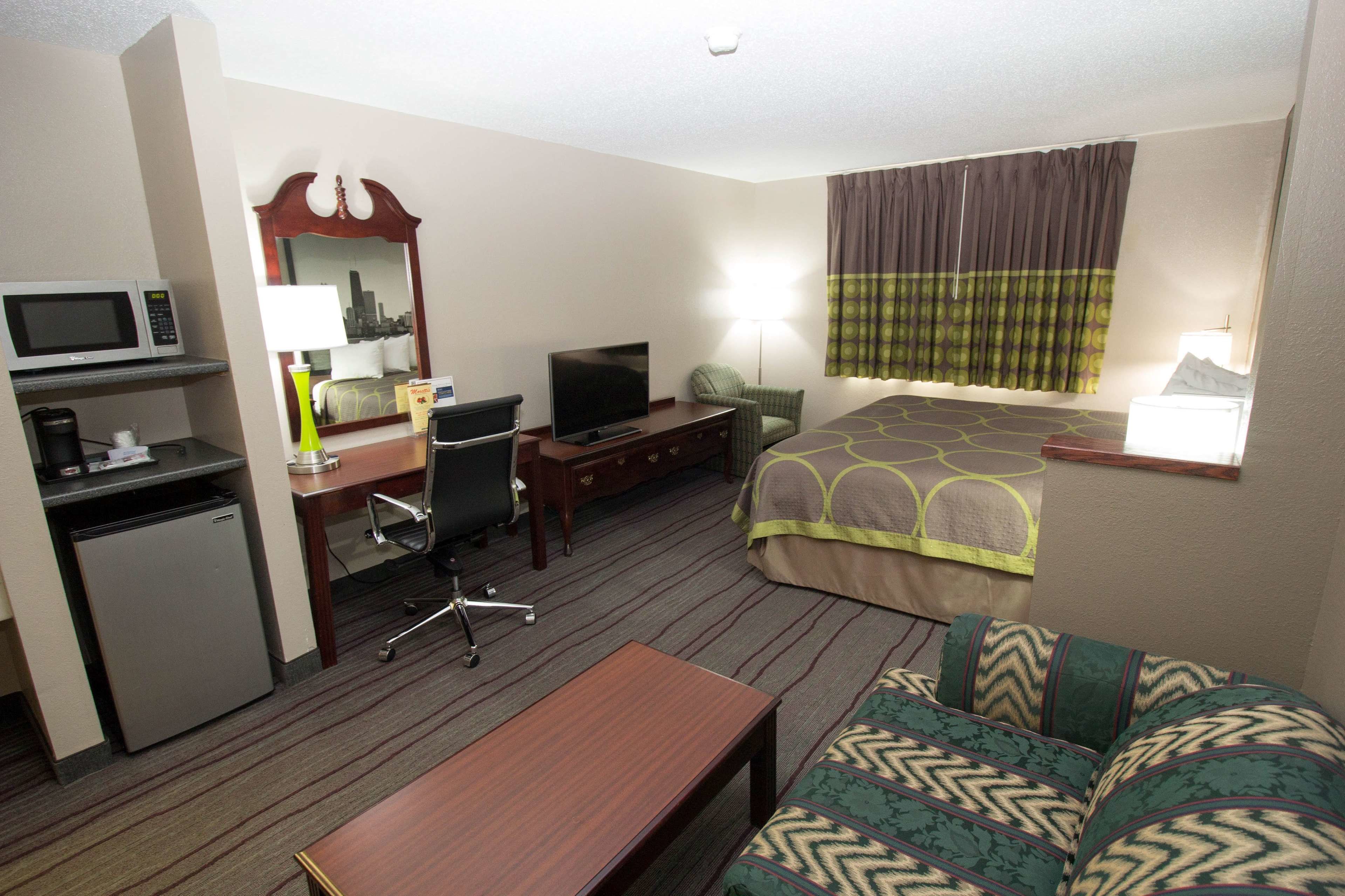 A hotel room with a bed, a desk with a computer, a television, a microwave, and a refrigerator.