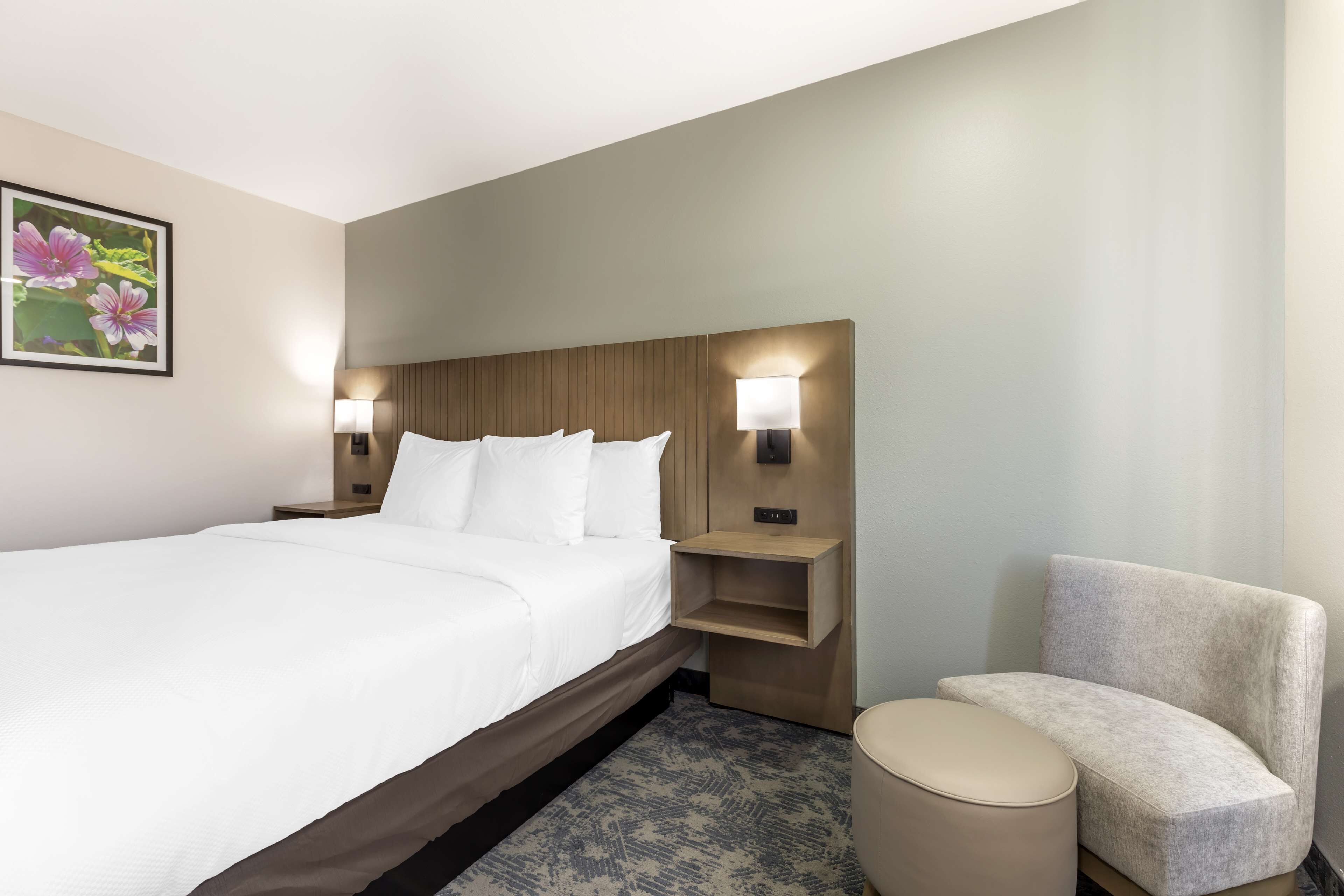 A hotel room with a large bed, two bedside tables with lamps, a small sofa, and a round ottoman.