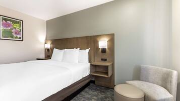 A hotel room with a large bed, two bedside tables with lamps, a small sofa, and a round ottoman.