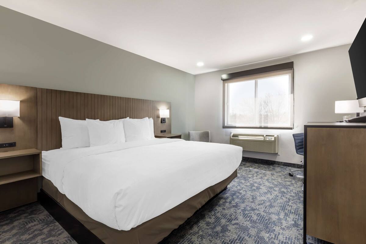Ein Hotelzimmer mit einem großen Bett, Nachttischen, einem Schreibtisch und einem Fenster mit Blick.