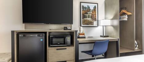 A hotel room with a bed, a desk with a chair, a television, a microwave, a refrigerator, a wardrobe, and a framed picture on the wall.