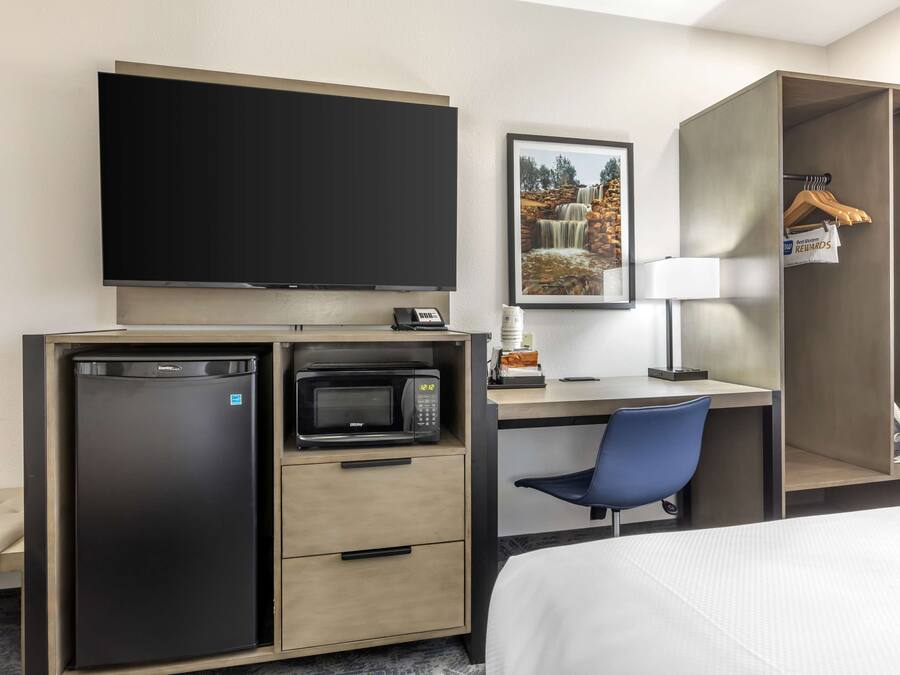 Une chambre d’hôtel comprenant un lit, un bureau avec une chaise, une télévision, un four à micro-ondes, un réfrigérateur, une armoire et un tableau encadré au mur.