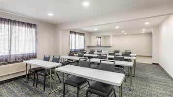 A conference room with multiple tables and chairs, large windows with curtains, and a carpeted floor.