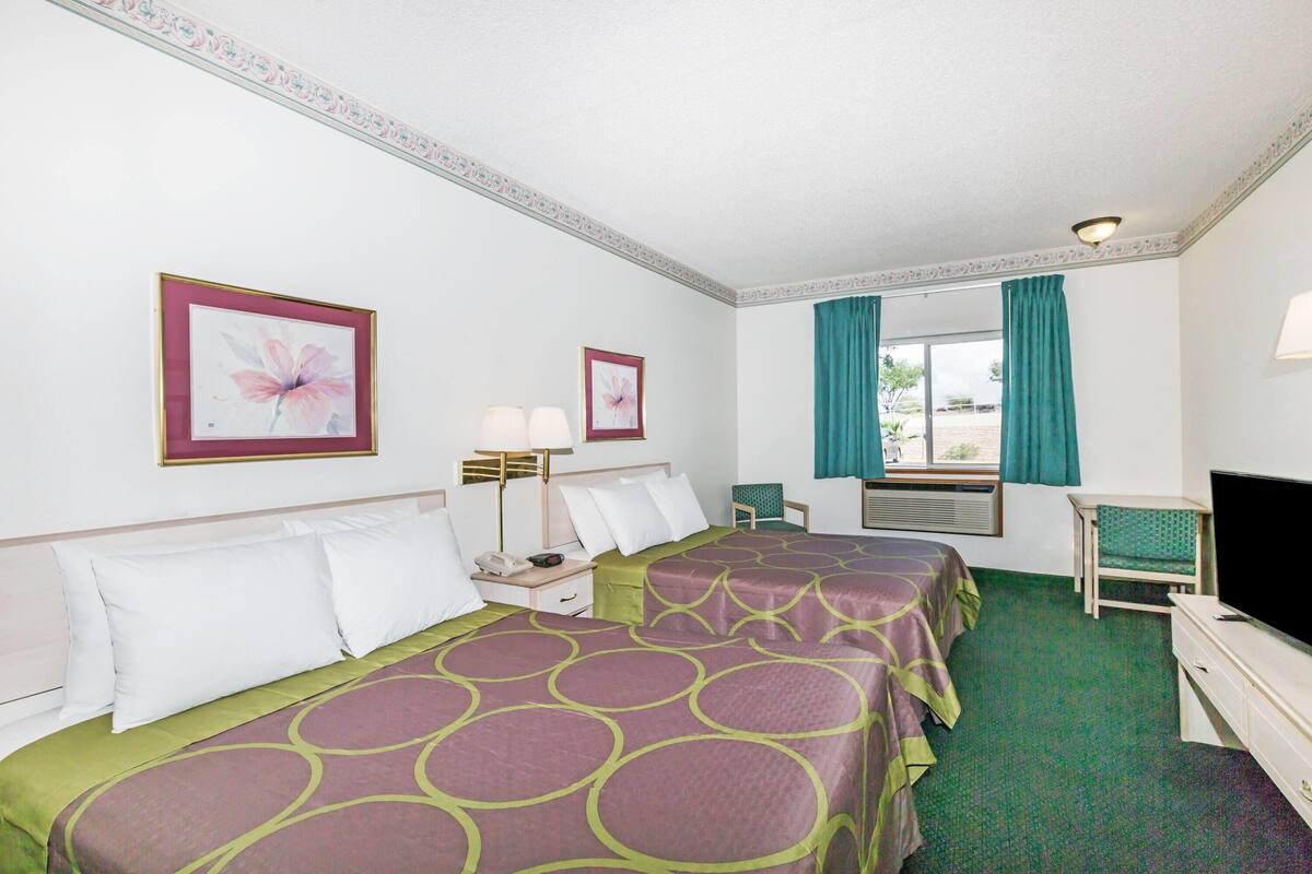 A hotel room with two beds, a desk, a TV, and a window with curtains.