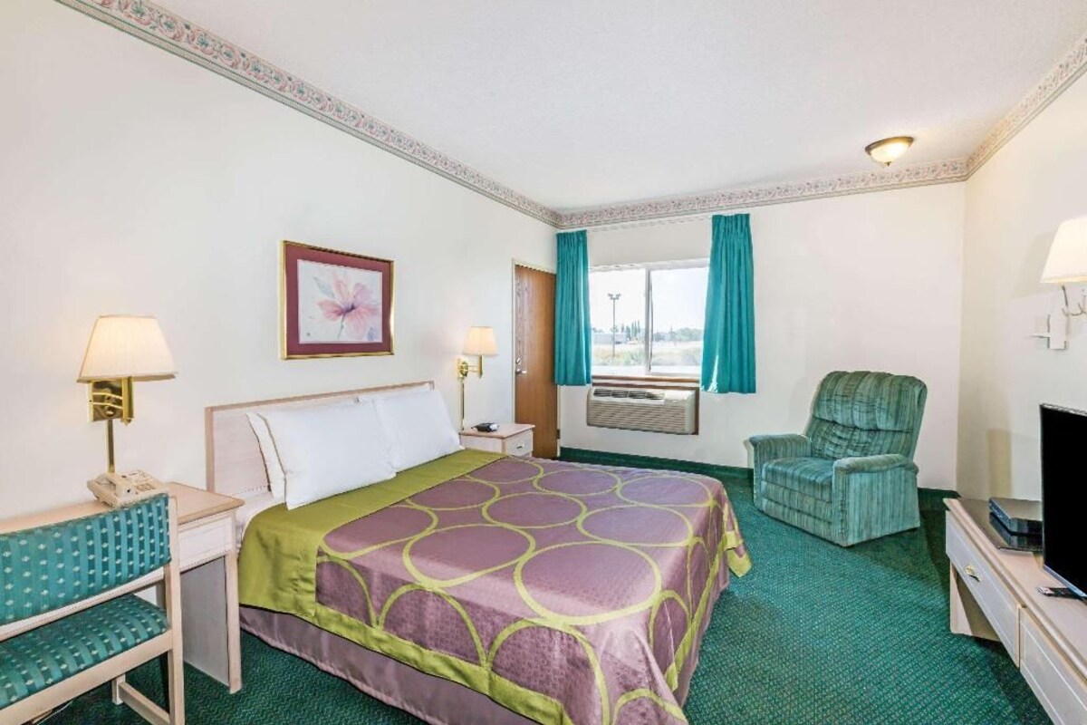 A hotel room with a bed, a desk, a chair, a television, and a window with curtains.