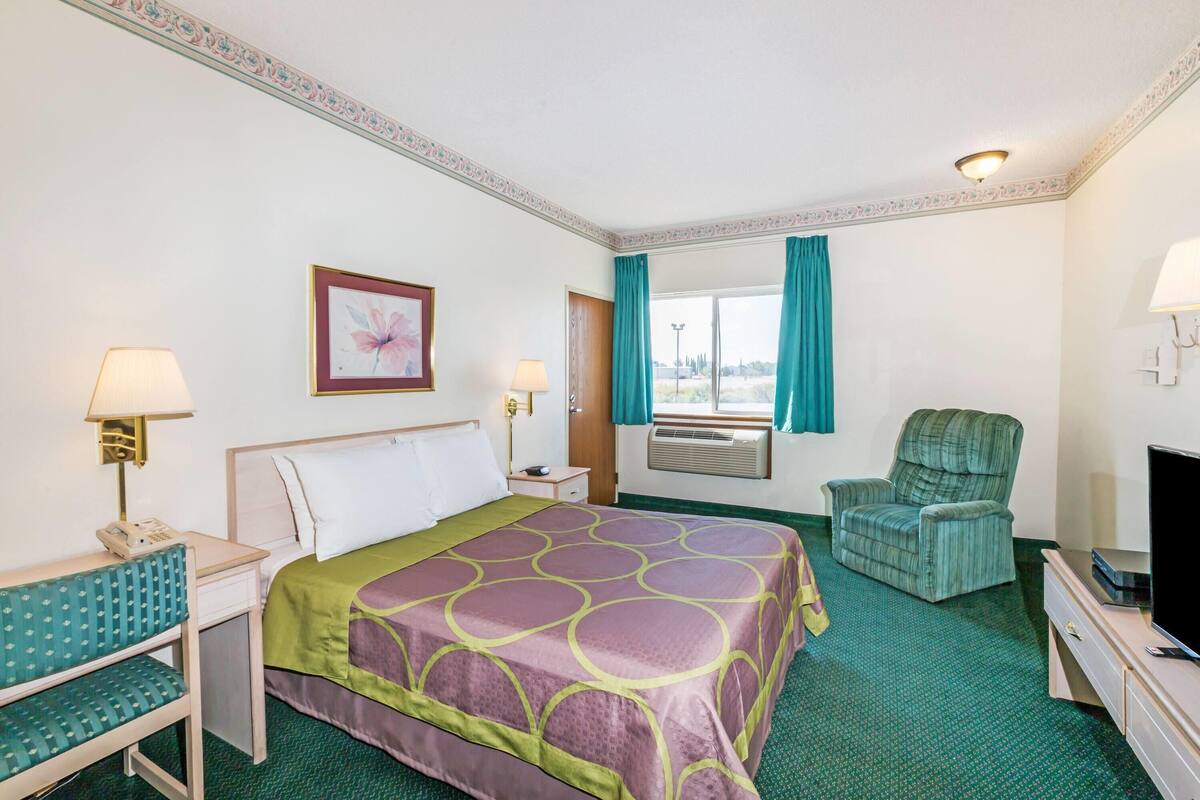 A hotel room with a bed, a desk, a chair, a television, and a window with curtains.