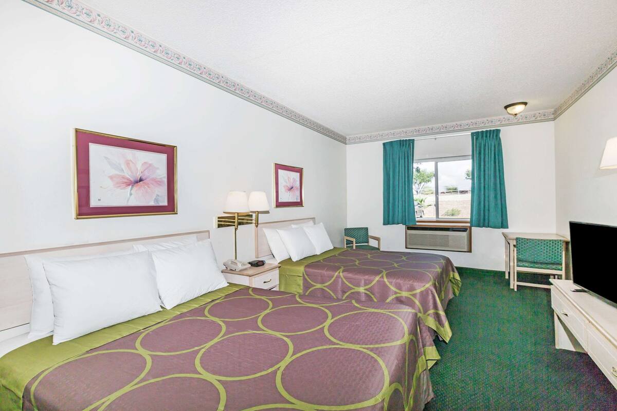 A hotel room with two beds, a desk, a television, and a window with curtains.