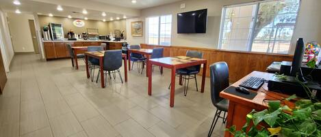 Un espace repas avec des tables et des chaises en bois, un comptoir avec une machine à café et un téléviseur fixé au mur.