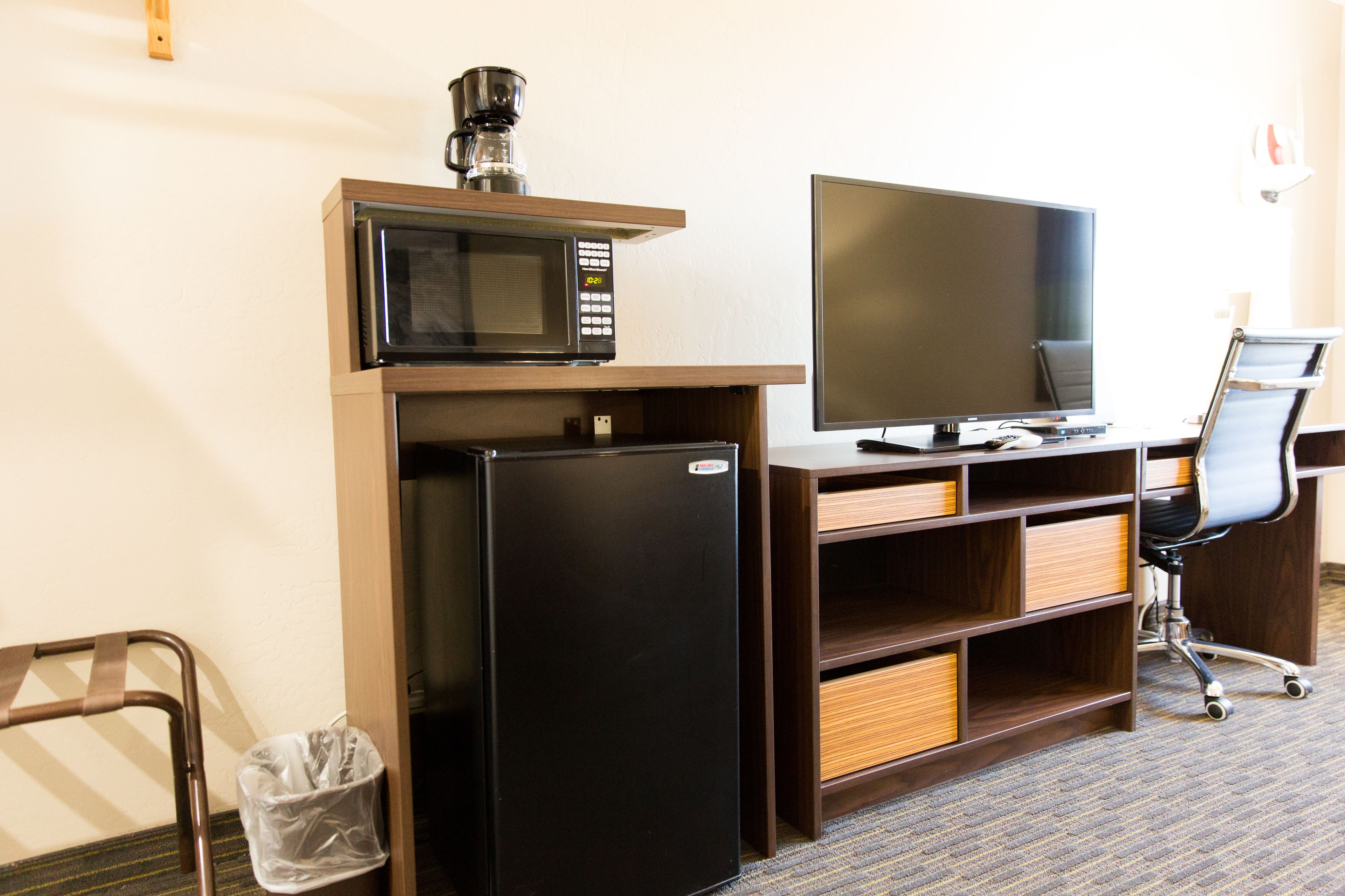 A compact hotel room with a kitchenette, including a microwave, refrigerator, and coffee maker.