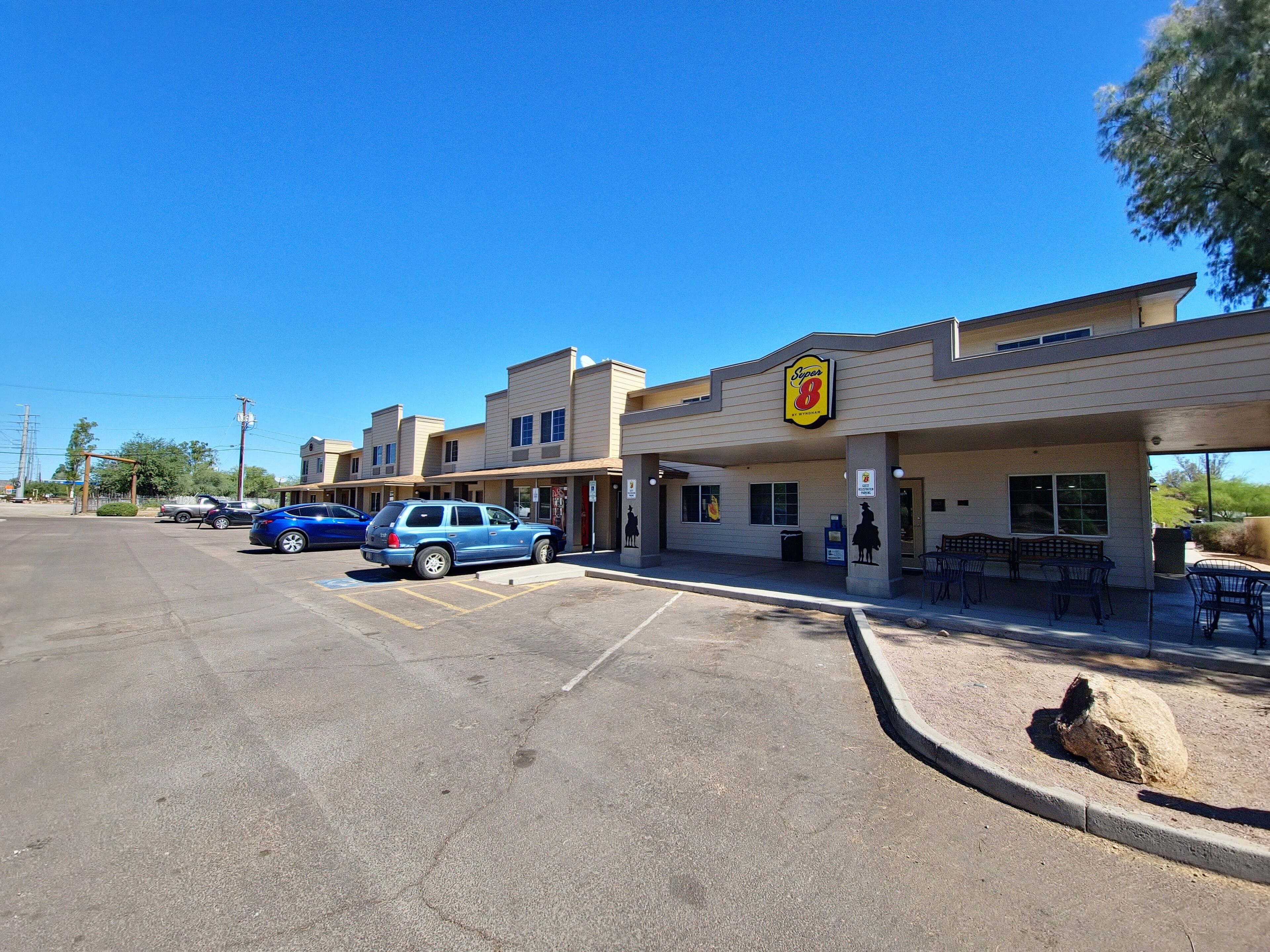 A Super 8 motel with a parking lot, outdoor seating, and a clear blue sky.
