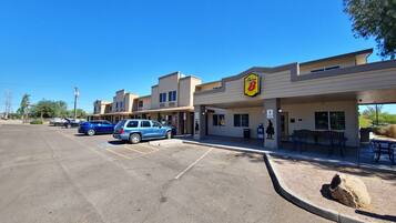 Un motel Super 8 con estacionamiento, asientos exteriores y un cielo azul despejado.