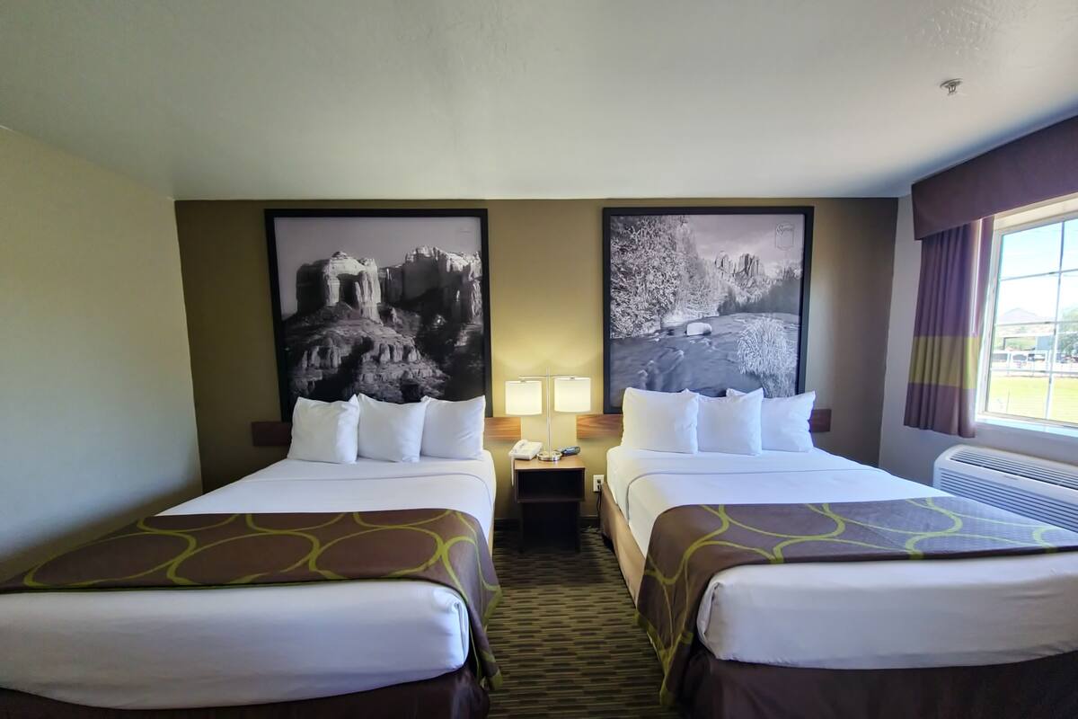Une chambre d’hôtel avec deux lits, une table de chevet avec une lampe et deux grandes images encadrées au mur.