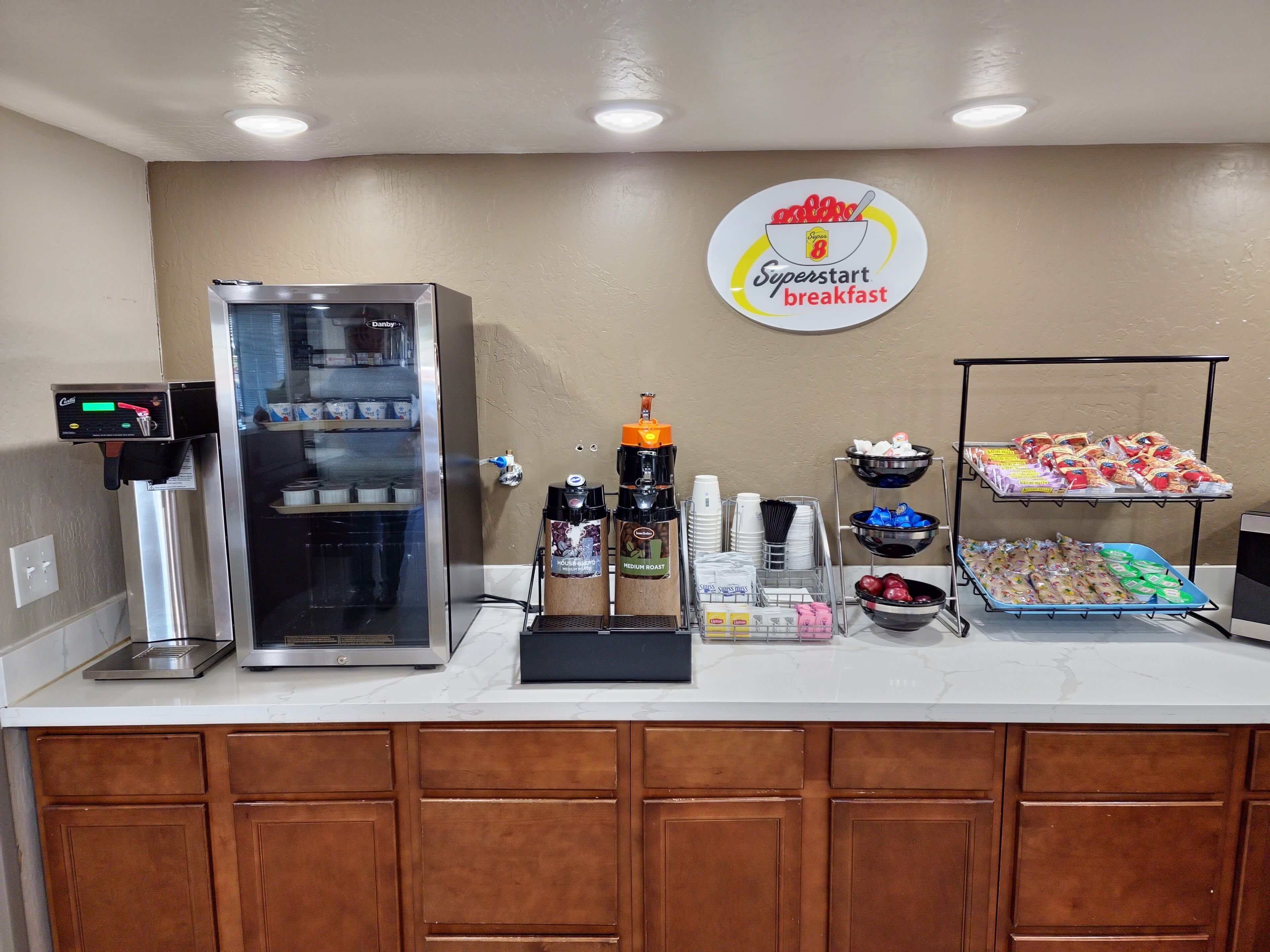 Una barra de desayuno con refrigerador, cafetera y un cartel que dice 'Superstart breakfast'.