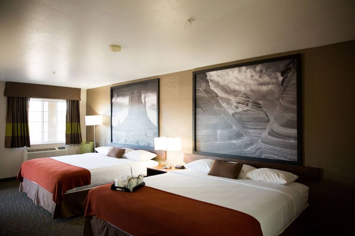 Une chambre d’hôtel avec deux lits, une grande fenêtre avec des rideaux, un climatiseur fixé au mur et deux grands tableaux encadrés.