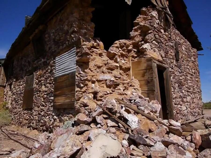 A rustic stone building with a partially collapsed roof and a large open doorway.