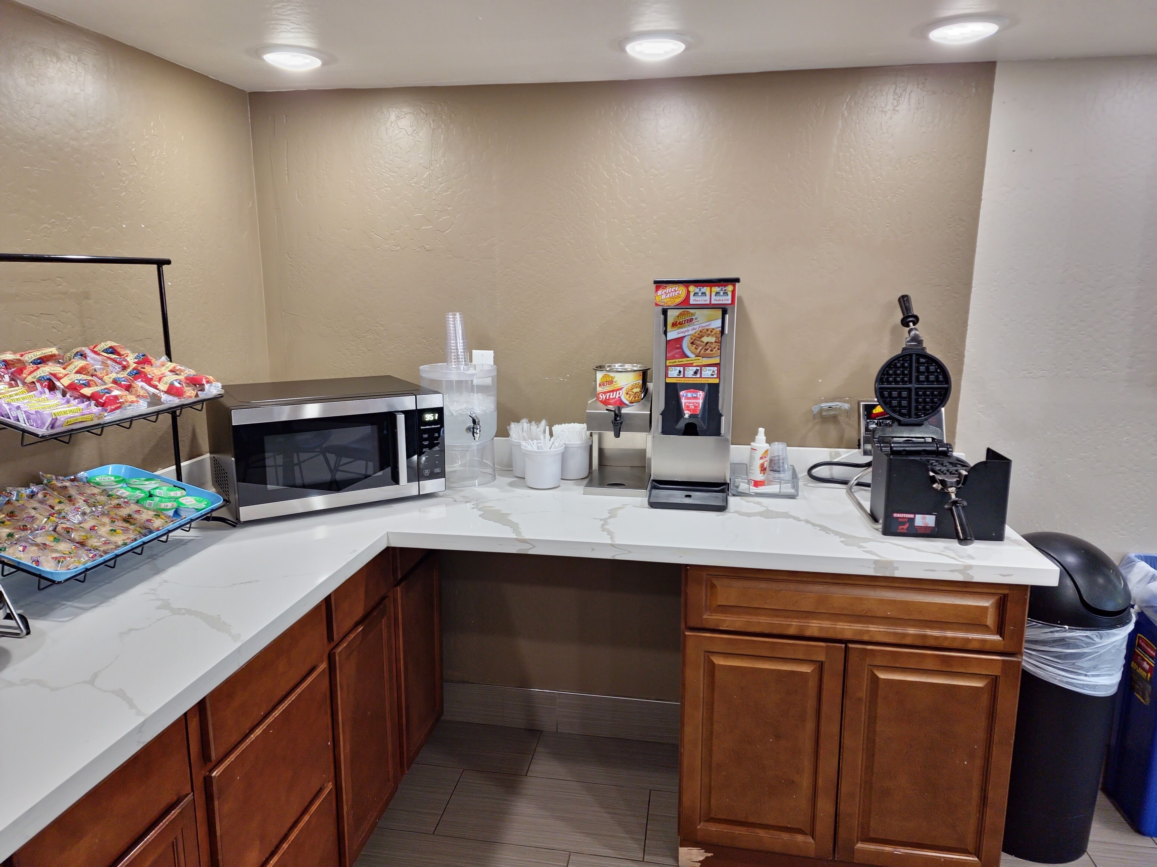A kitchenette with a microwave, coffee machine, waffle maker, and snack dispensers.