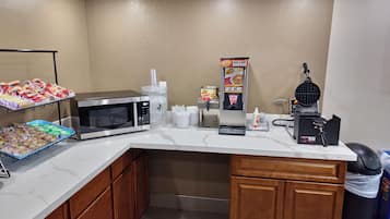 A kitchenette with a microwave, coffee machine, waffle maker, and snack dispensers.