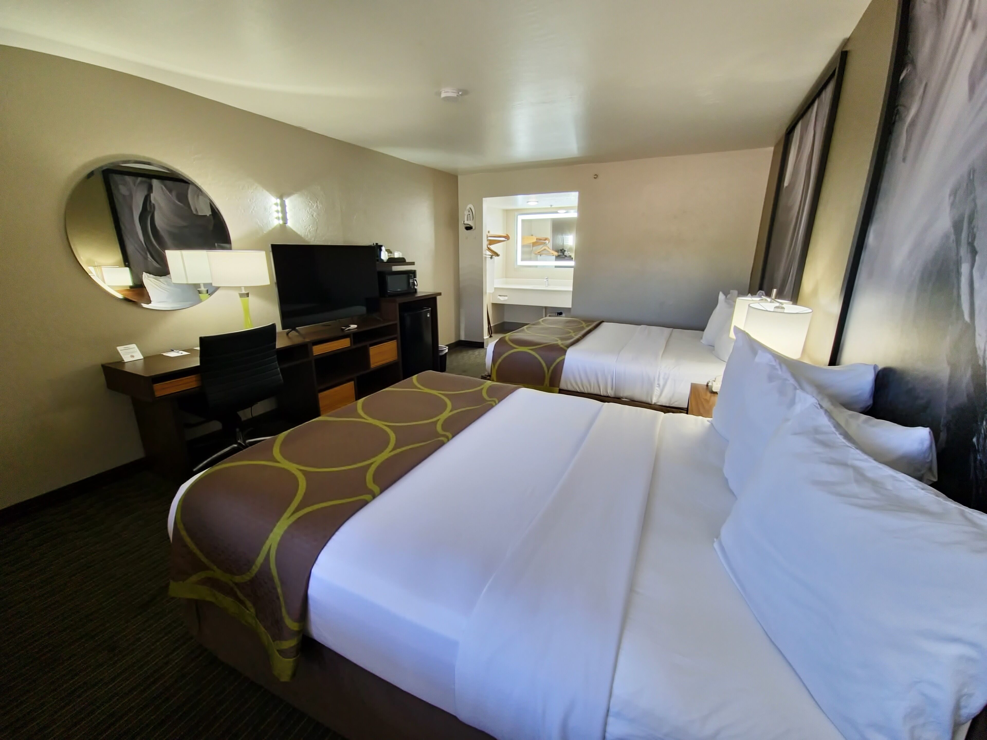 A hotel room with two beds, a desk with a computer, a television, and a mirror.