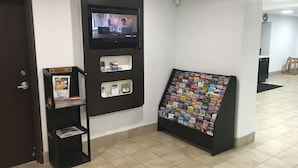 A reception area with a digital screen displaying a video, a bulletin board with various pamphlets, and a small shelf with a framed photo and some items. - Americas Best Value Inn Apache Junction (Apache Junction)