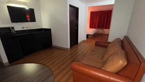 A living room with a brown leather sofa, a wooden dining table, and a kitchen area with a black countertop and a flat-screen TV mounted above it. - Americas Best Value Inn Apache Junction (Apache Junction)