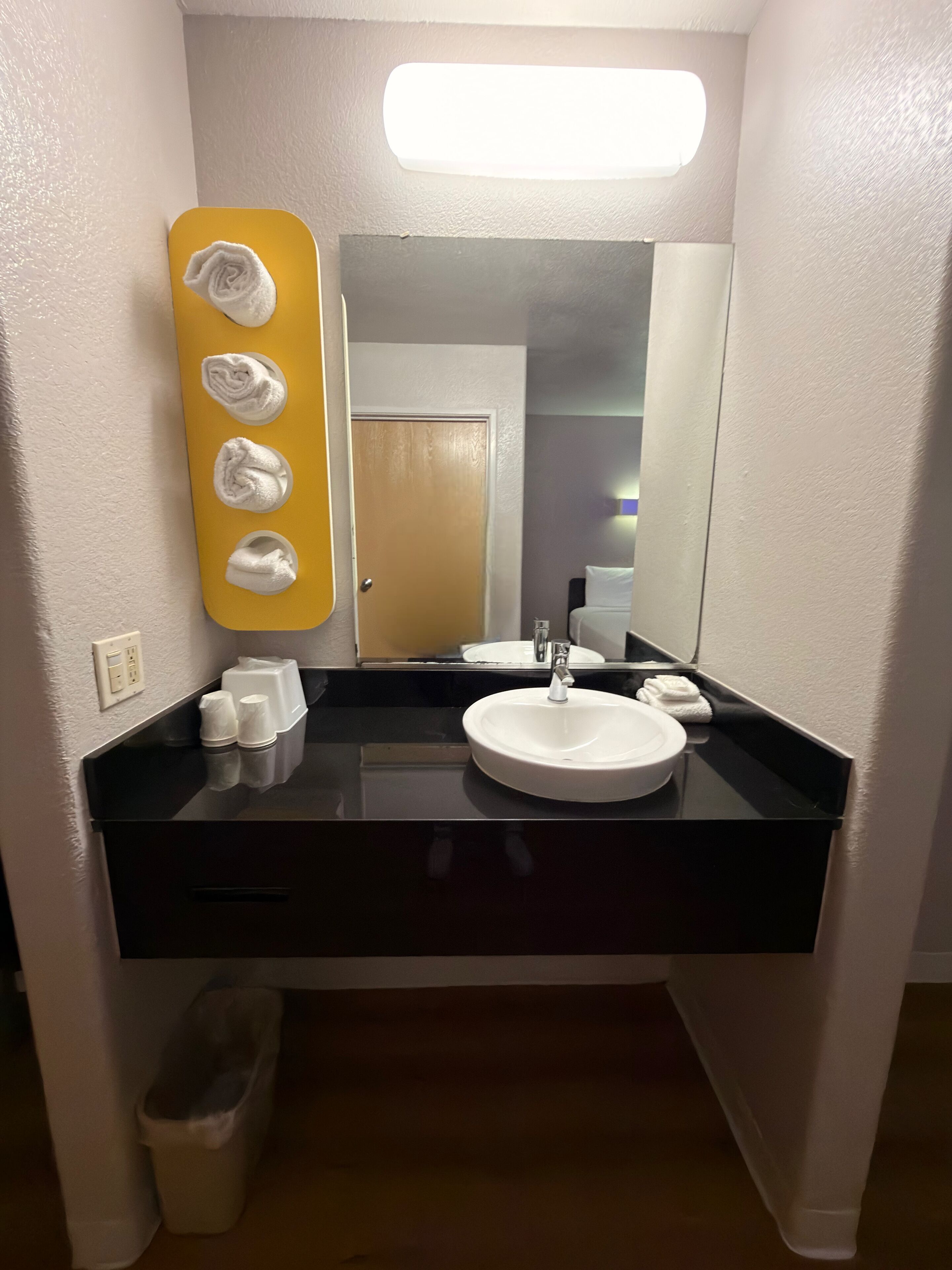 A bathroom with a black countertop, a white sink, a mirror, and a yellow towel warmer with towels.
