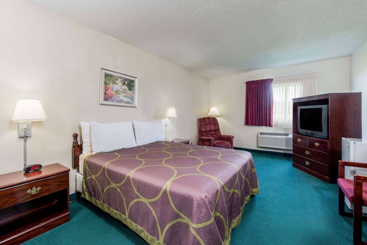 A hotel room with a bed, a TV, a chair, a desk, and a picture on the wall.