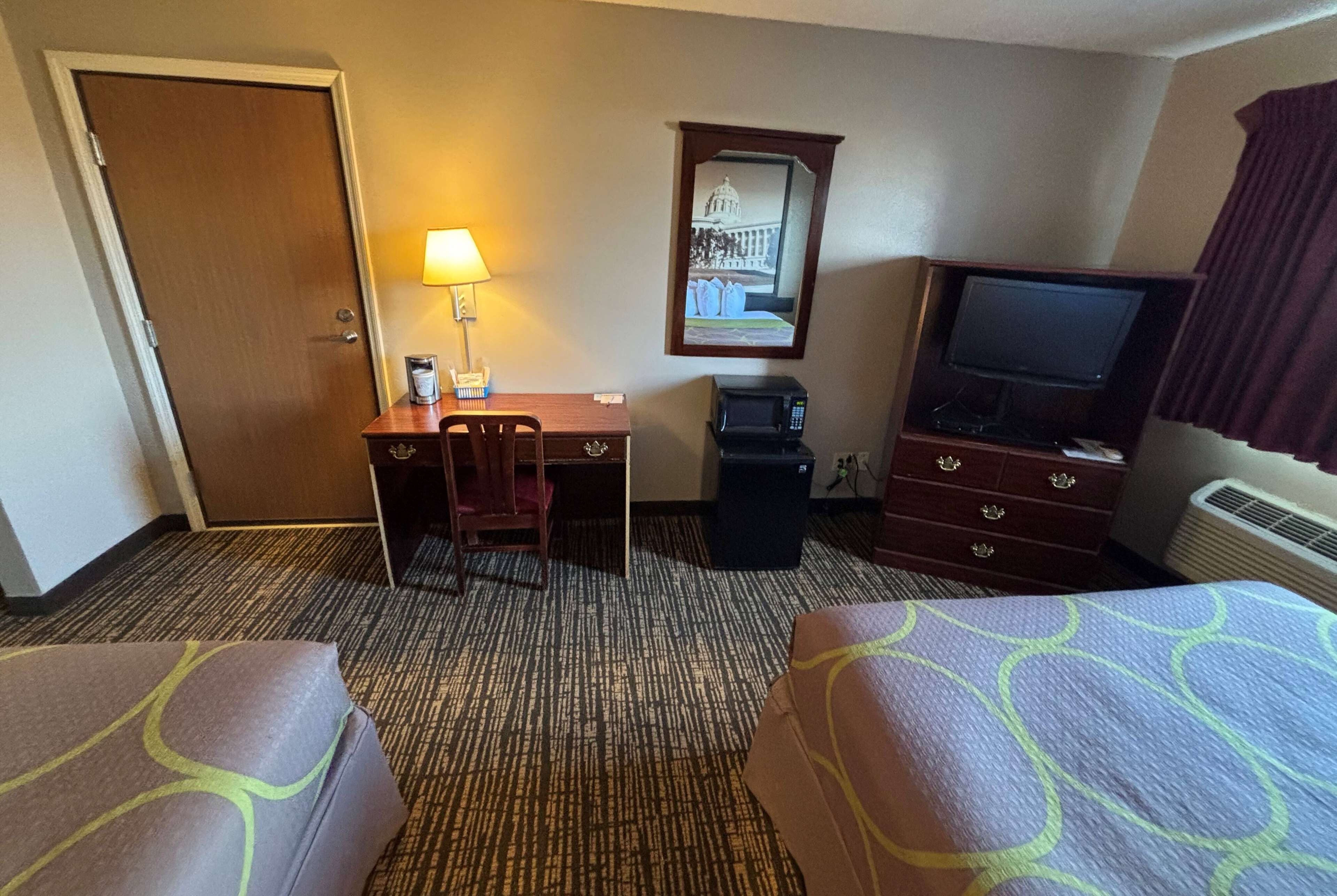 Ein Hotelzimmer mit zwei Betten, einem Schreibtisch mit Stuhl, einem Fernseher, einer Mikrowelle und einer Lampe.