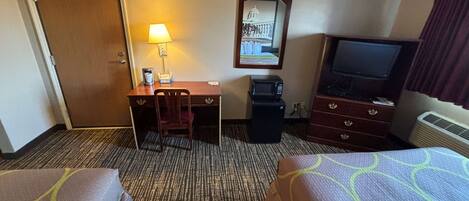 Una habitación de hotel con dos camas, un escritorio con silla, televisor, microondas y lámpara.