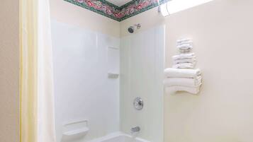 Une salle de bain avec une baignoire, une douche et des toilettes. Des serviettes sont pliées et empilées sur un porte-serviettes.