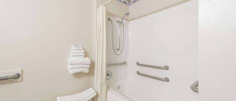 A bathroom with a bathtub, a shower, a toilet, and a handrail.