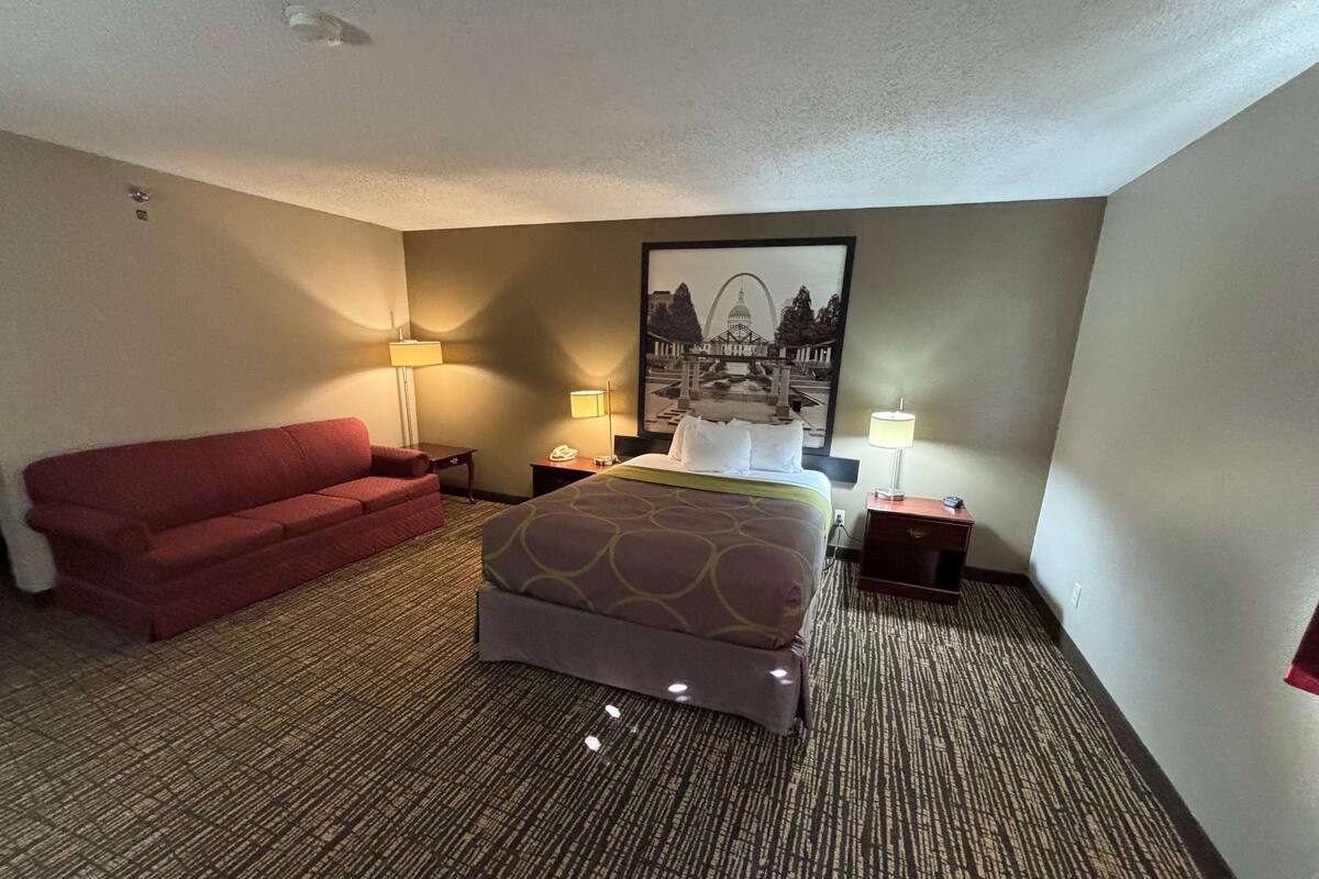 A hotel room with a bed, a red sofa, two bedside tables with lamps, and a framed picture on the wall.