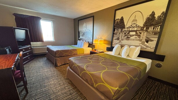 A hotel room with two beds, a desk, a TV, and a window.